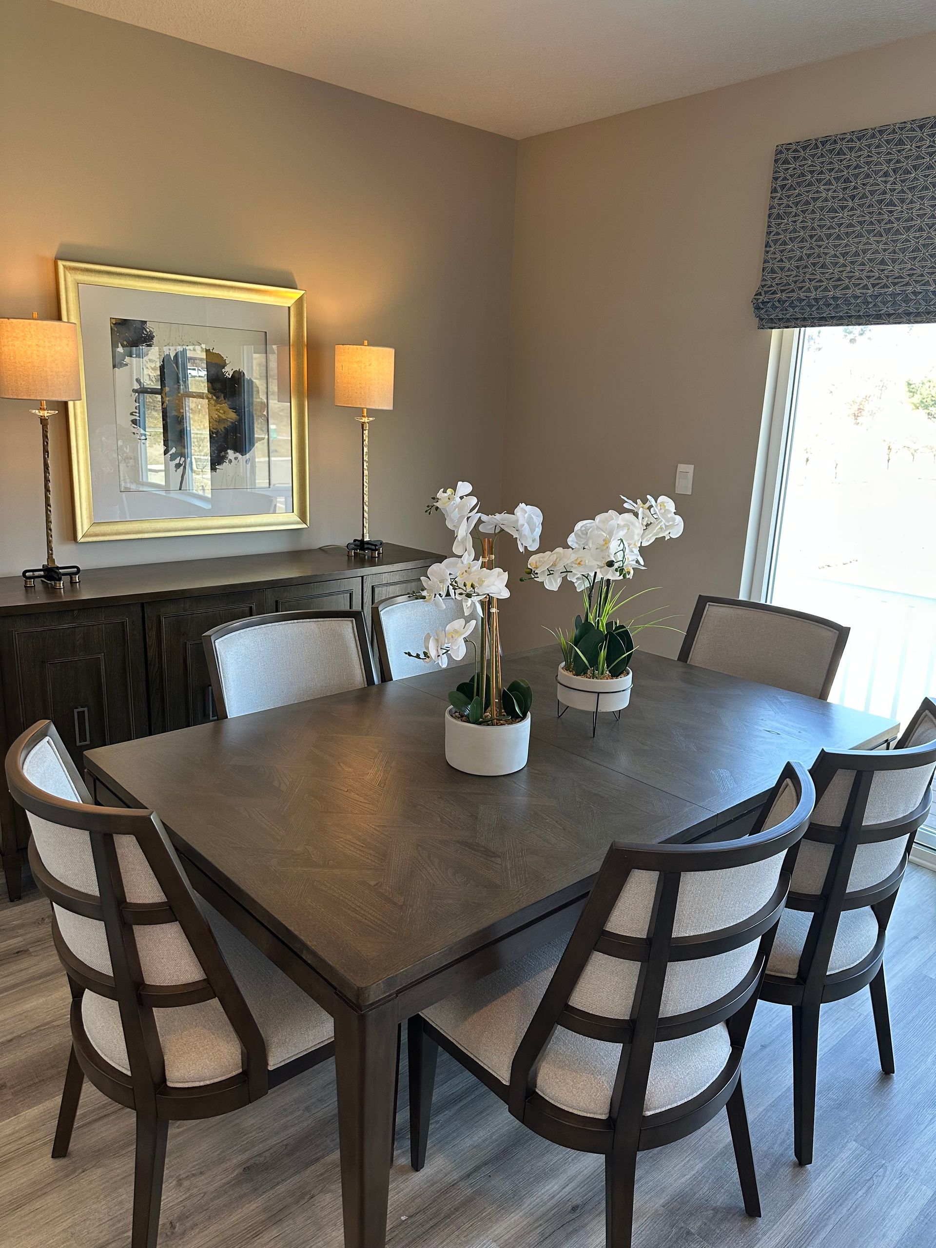 A dining room with a table and chairs and a vase of flowers on it.