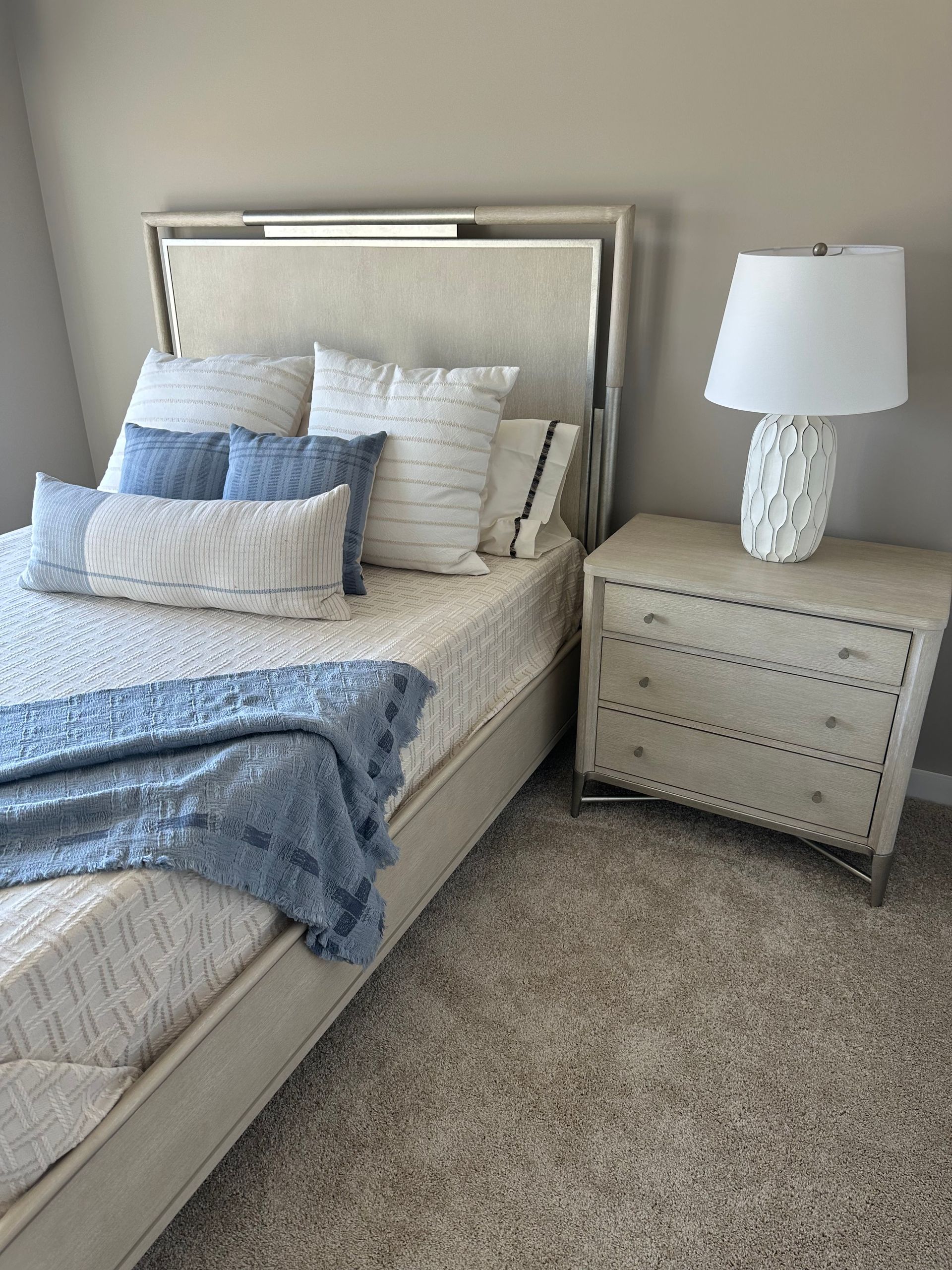 A bedroom with a bed, nightstand, lamp, and carpet.