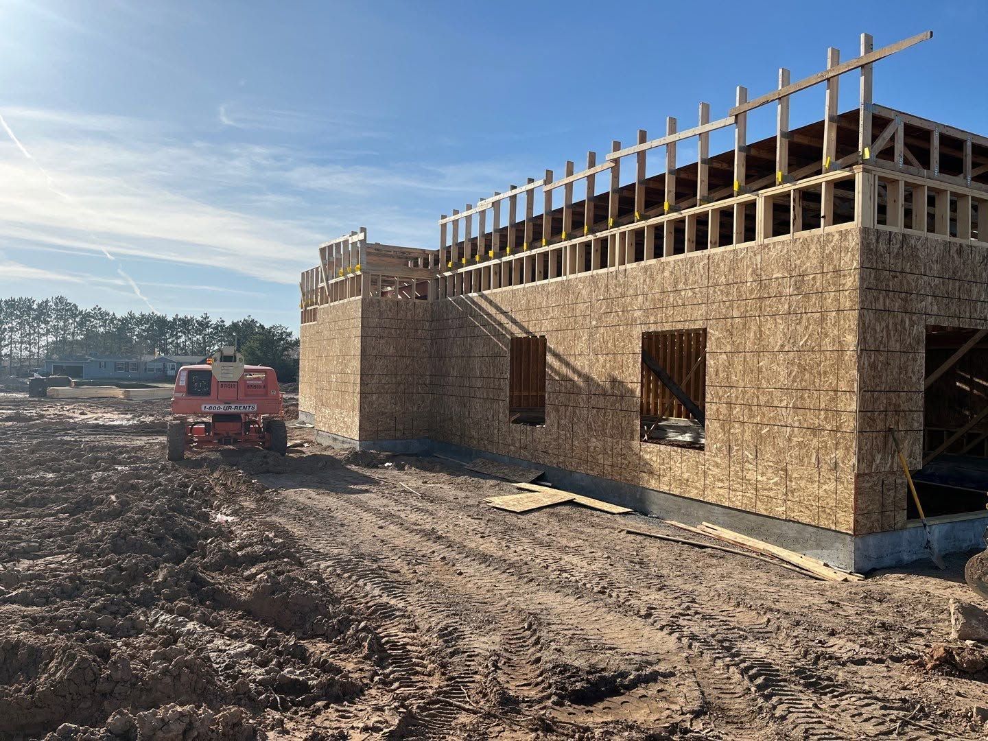 Construction site with a partially framed wooden building under a clear sky.