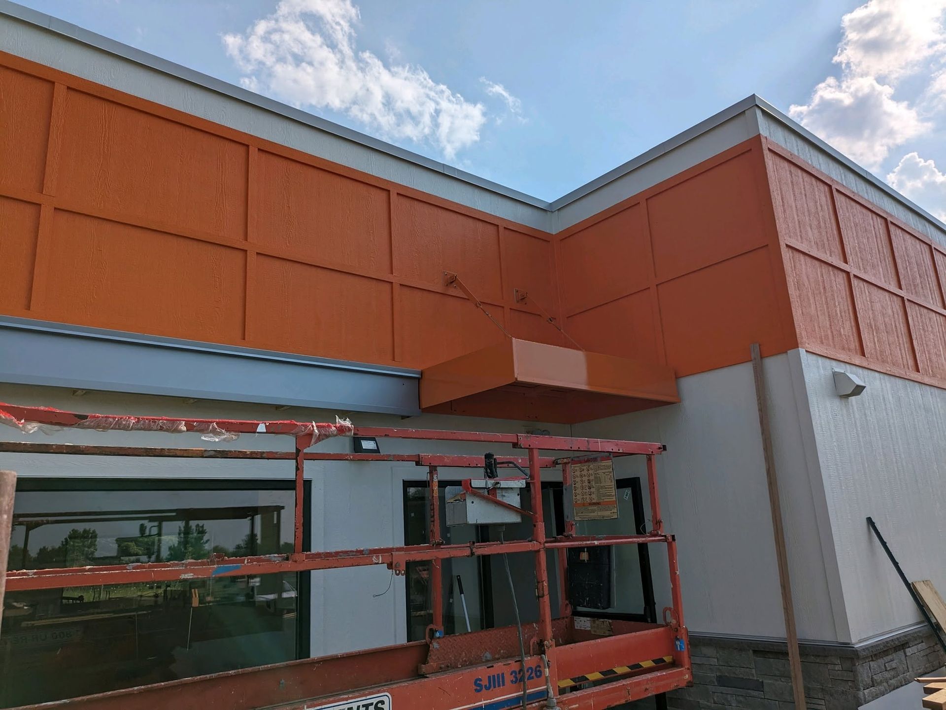 Orange-and-white building exterior with red scaffolding and a cloudy sky overhead