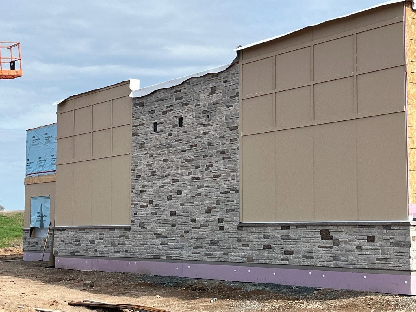 Exterior of a partly renovated building with tan panels, stone center, and purple base under a cloudy sky