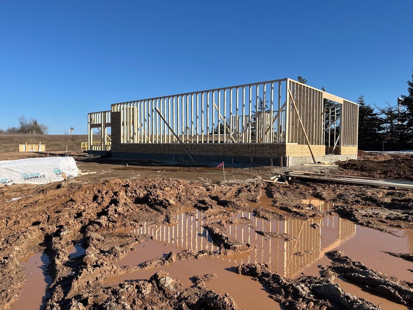 Partially framed building on a muddy construction site under a clear blue sky