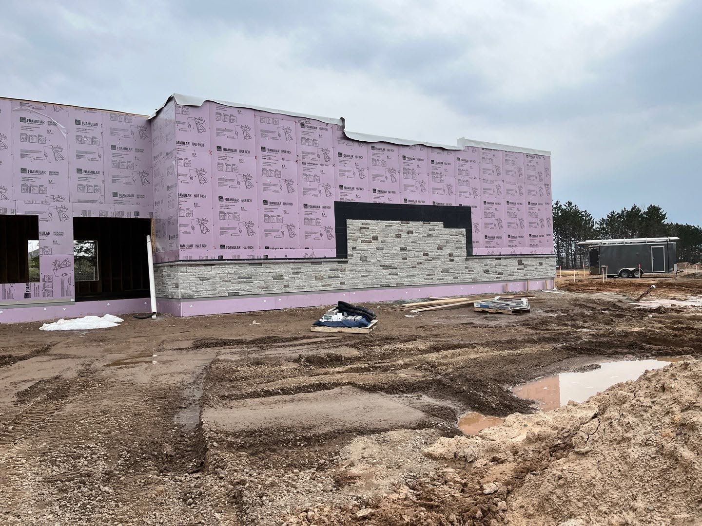Partially built pink house with dirt lot and construction materials in the foreground