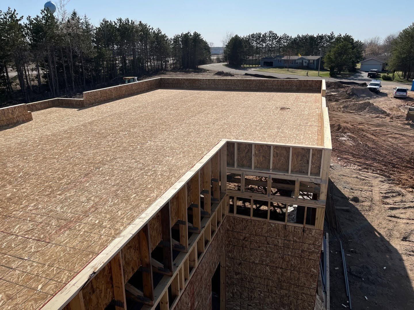 A building under construction with a large plywood roof and framed walls on a cleared site
