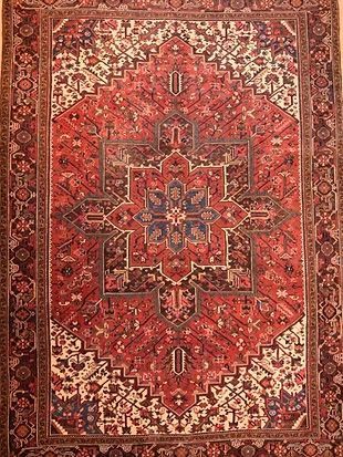 A red rug with a pattern on it is hanging on a wall.