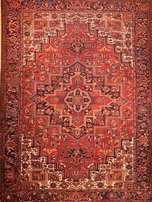 A red rug with a pattern on it is hanging on a wall.