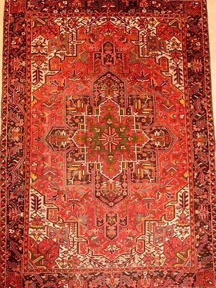A red rug with a pattern on it is hanging on a wall.