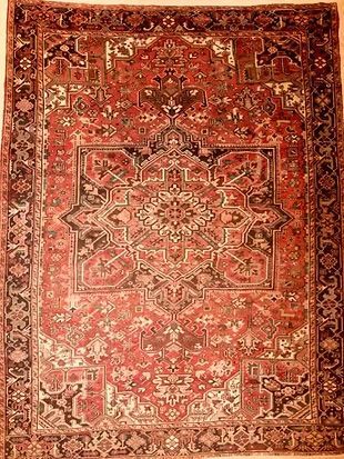 A red rug with a pattern on it is hanging on a wall.