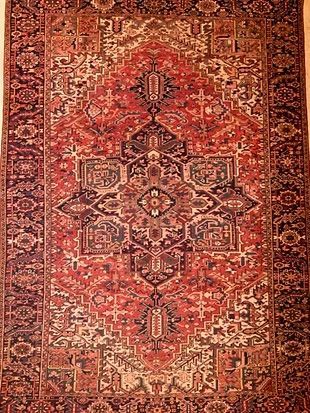 A red rug with a pattern on it is hanging on a wall.