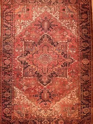 A red rug with a pattern on it is hanging on a wall.
