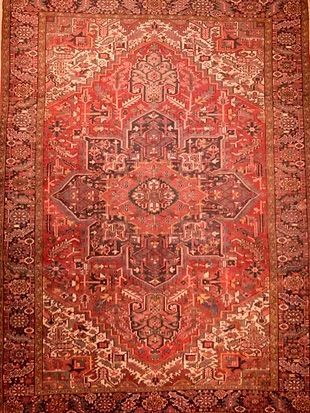 A red rug with a pattern on it is hanging on a wall.