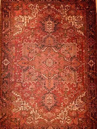 A red rug with a pattern on it is hanging on a wall.