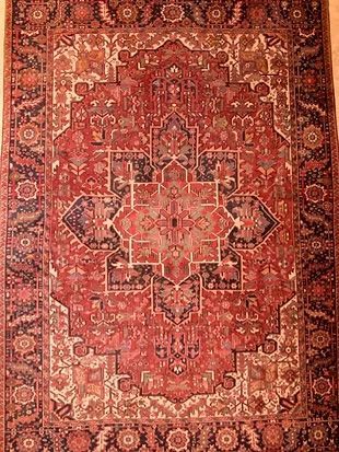 A red rug with a pattern on it is hanging on a wall.