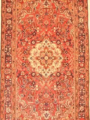 A red rug with a floral pattern on it is hanging on a wall.