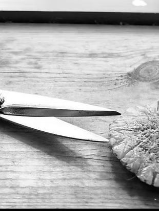 A pair of scissors is cutting a piece of bread on a wooden table.