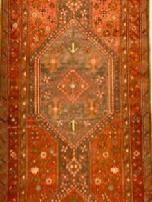 A red rug with a pattern on it is hanging on a wall.