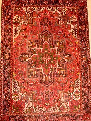 A red rug with a pattern on it is hanging on a wall.