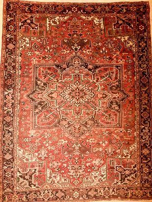 A red rug with a pattern on it is hanging on a wall.