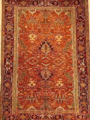 A red rug with a floral pattern on it is hanging on a wall.