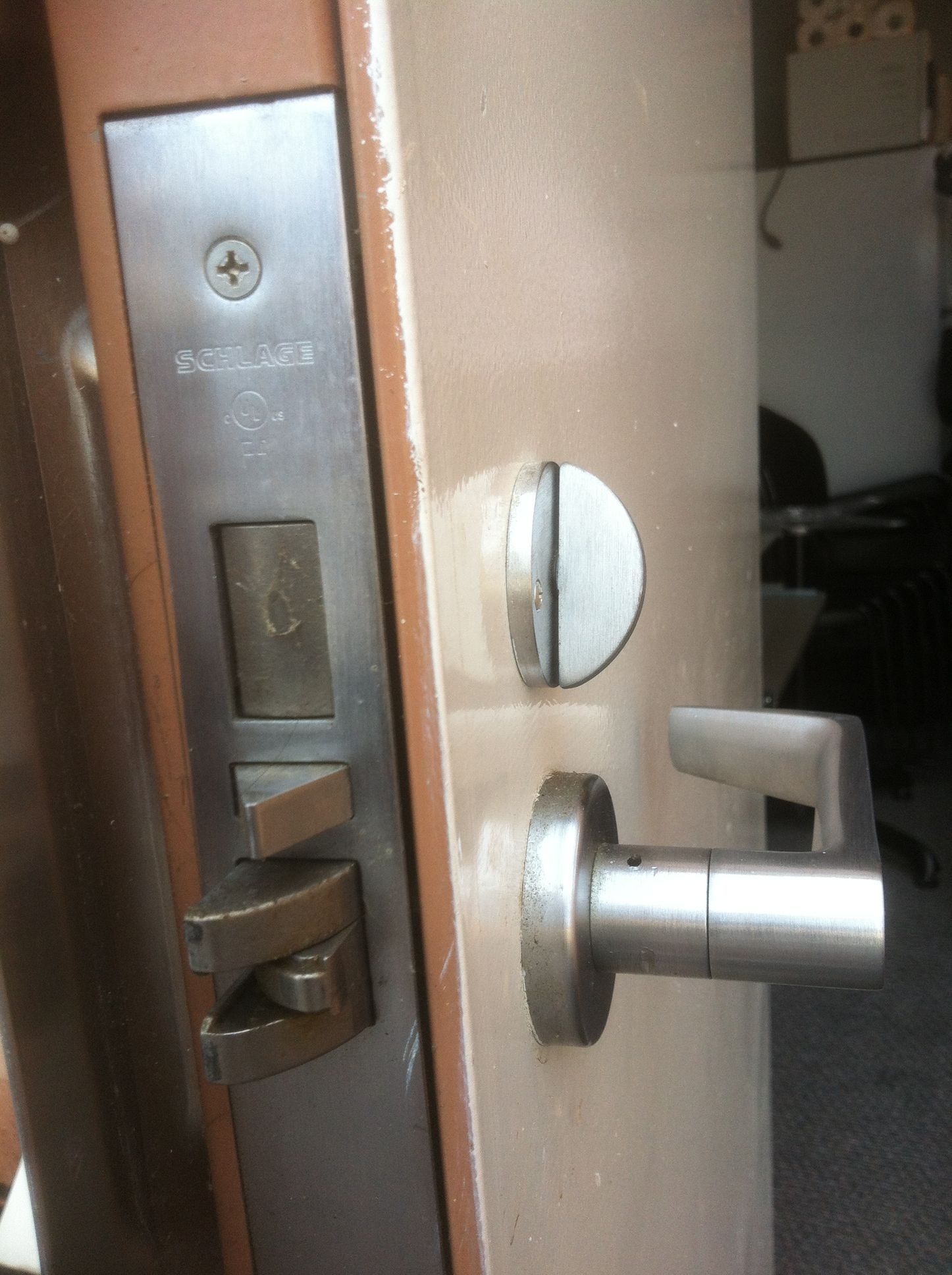Close-up of a door with a Schlage lock and lever handle. The lock is stainless steel. The door is tan.