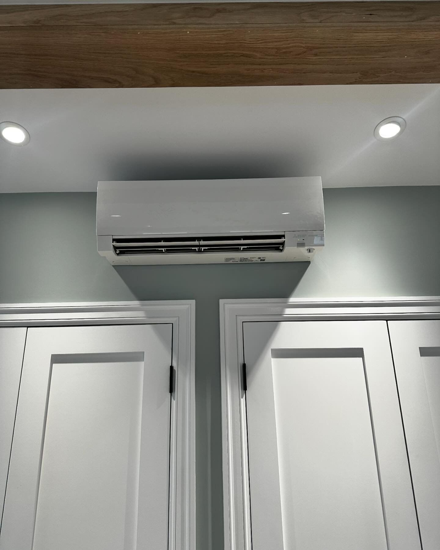 a white air conditioner is mounted to the wall above two white doors