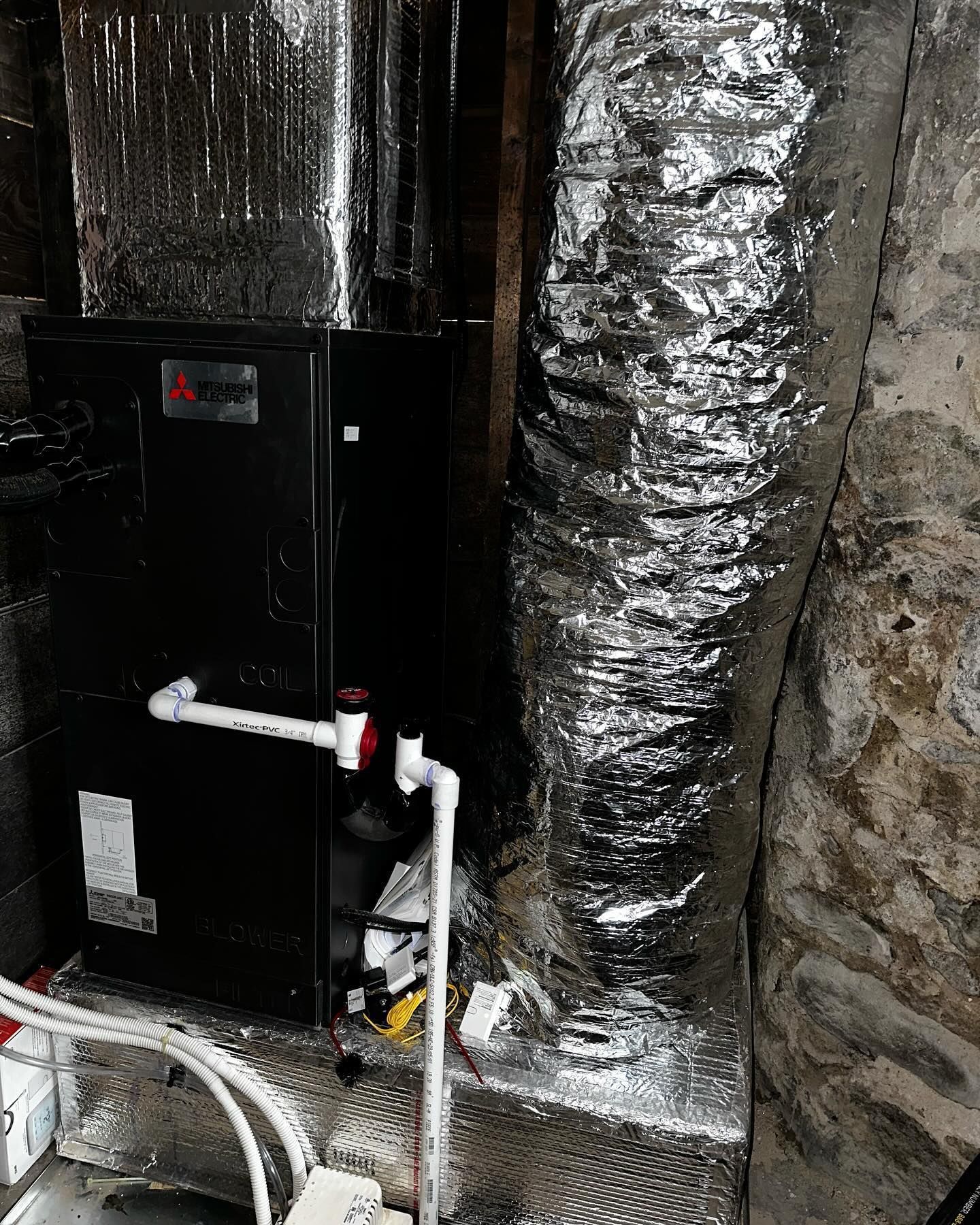 a black air conditioner is sitting next to a duct in a basement
