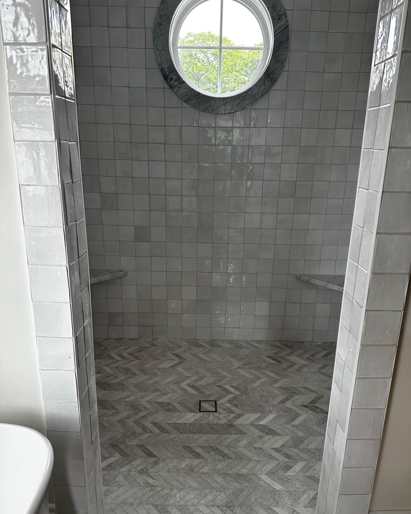 a bathroom with white tiles and a round window