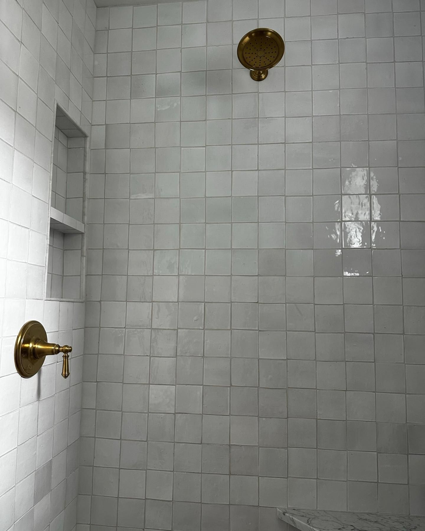 a shower with white tiles and a brass shower head