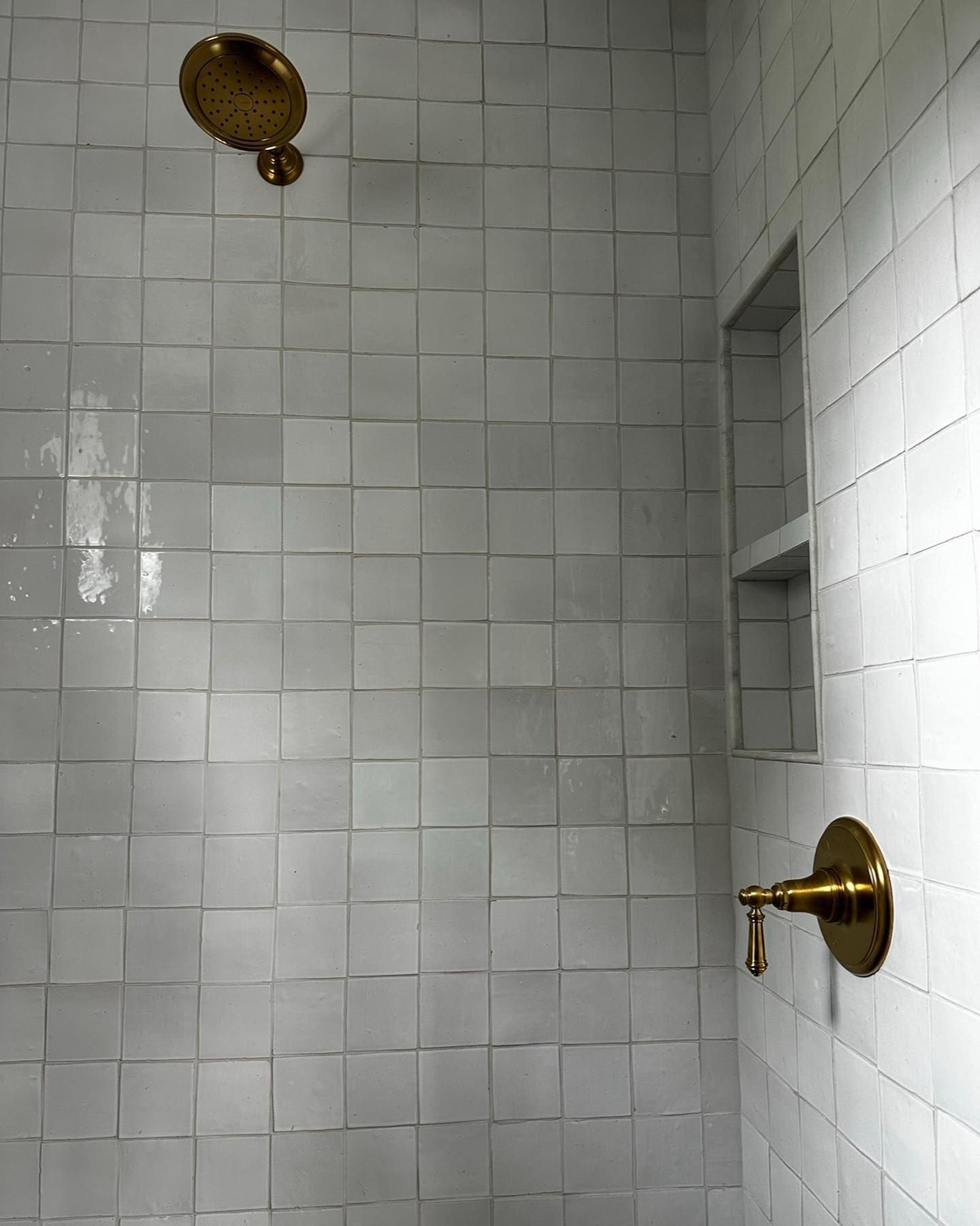 a shower with white tiles and a brass shower head