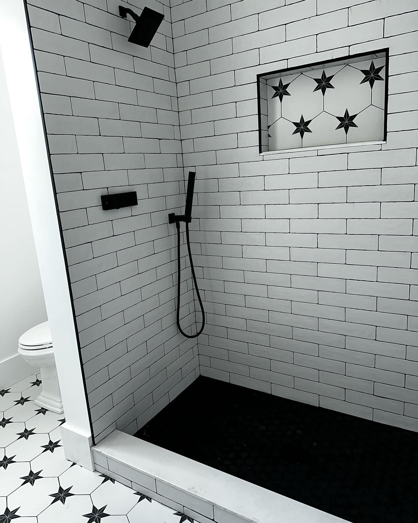 a black and white photo of a shower with white tiles and a black floor