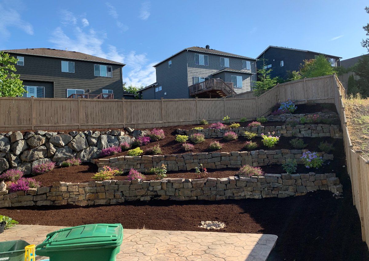 A green trash can is sitting in front of a stone wall.