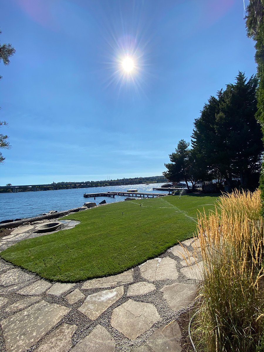 A stone walkway leading to a lake with a lot of grass and trees.