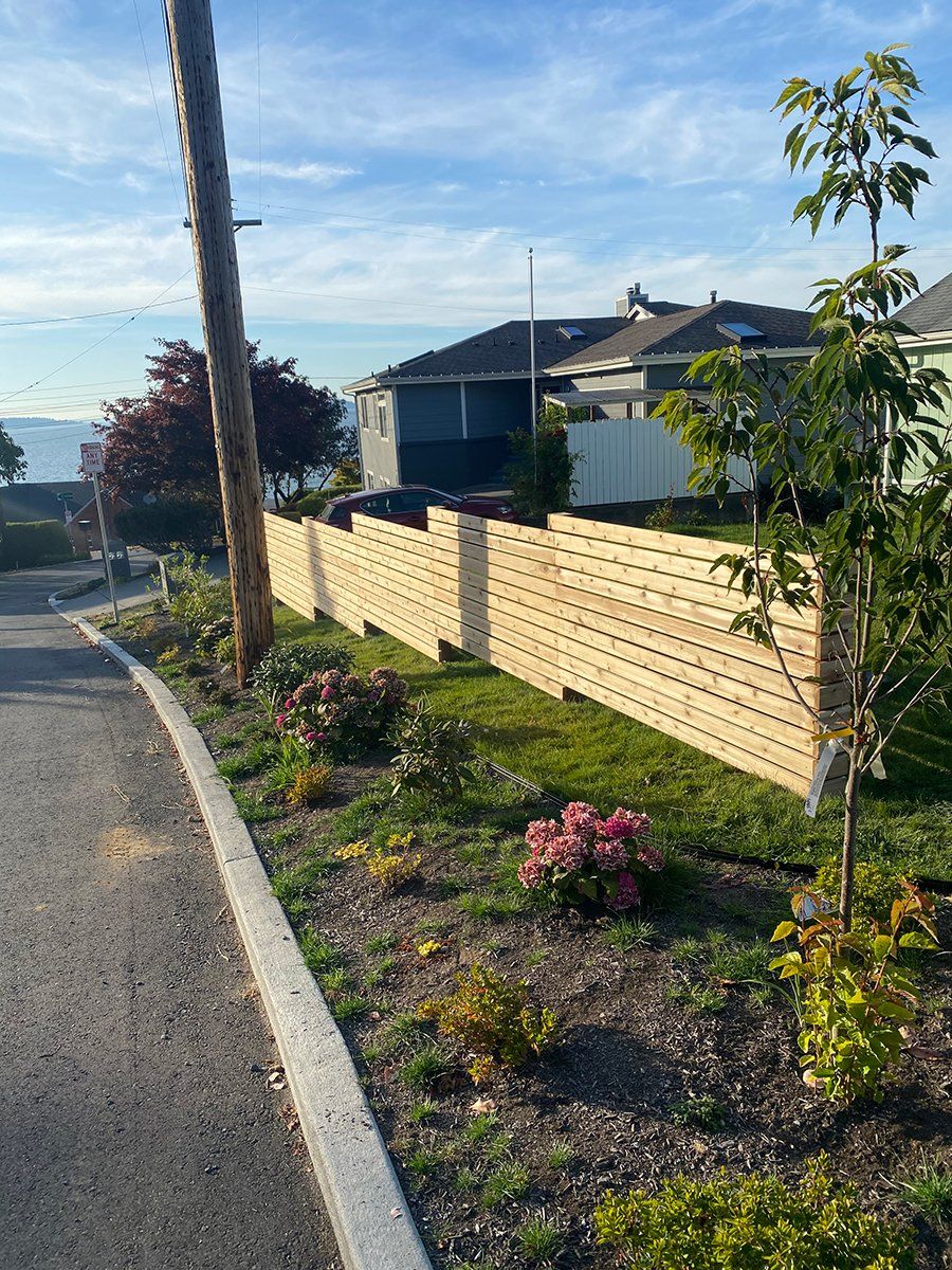 A wooden fence surrounds a lush green yard next to a road.