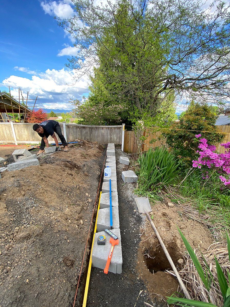 A man is working on a concrete wall in a garden.