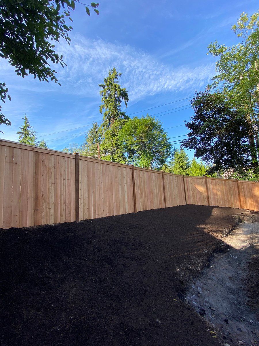 A wooden fence surrounds a pile of dirt in a backyard.