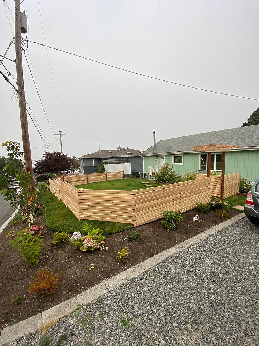 A car is parked in front of a house with a wooden fence.