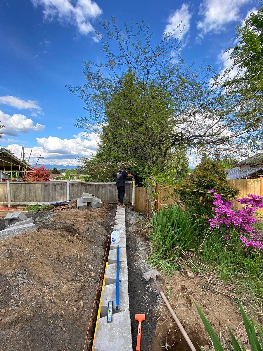 A man is standing next to a concrete wall in a garden.