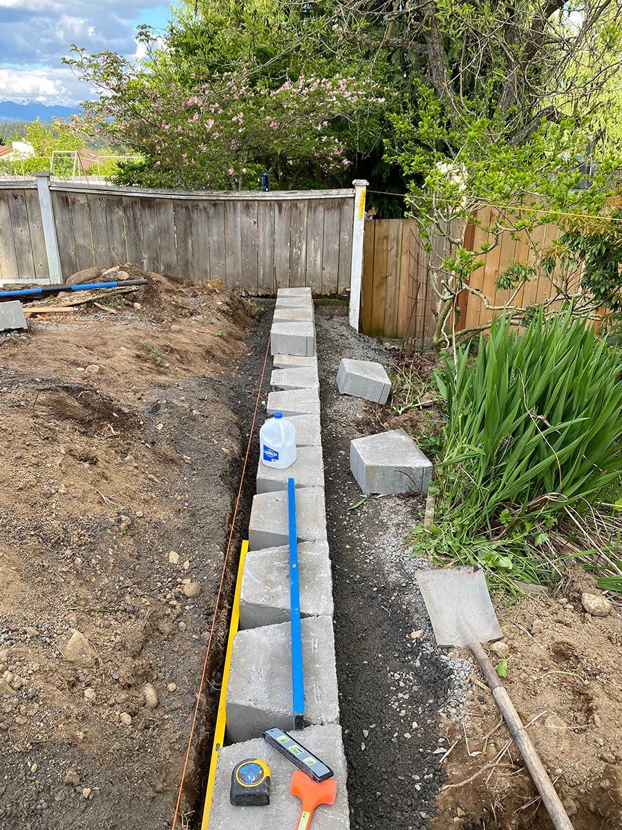 A brick wall is being built in a backyard next to a wooden fence.