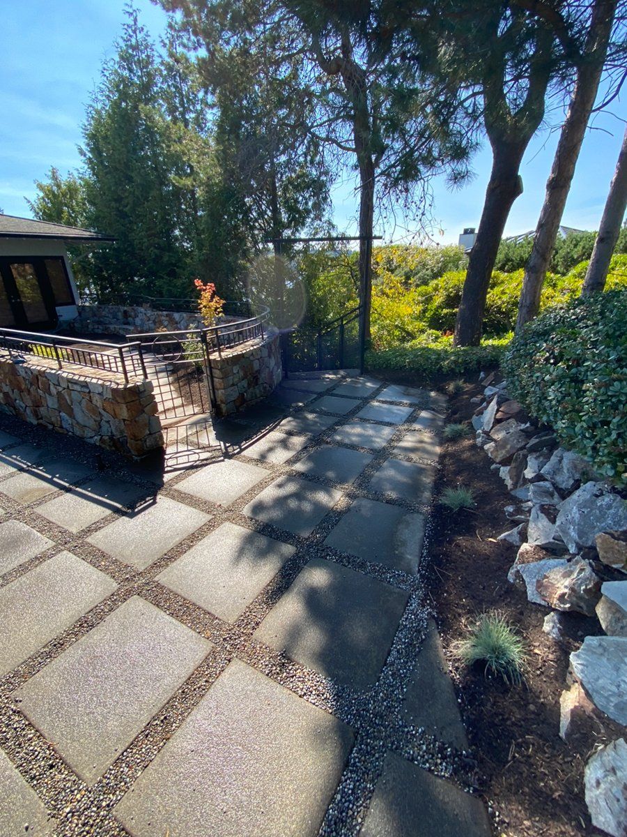 A stone walkway leading to a house with trees in the background.