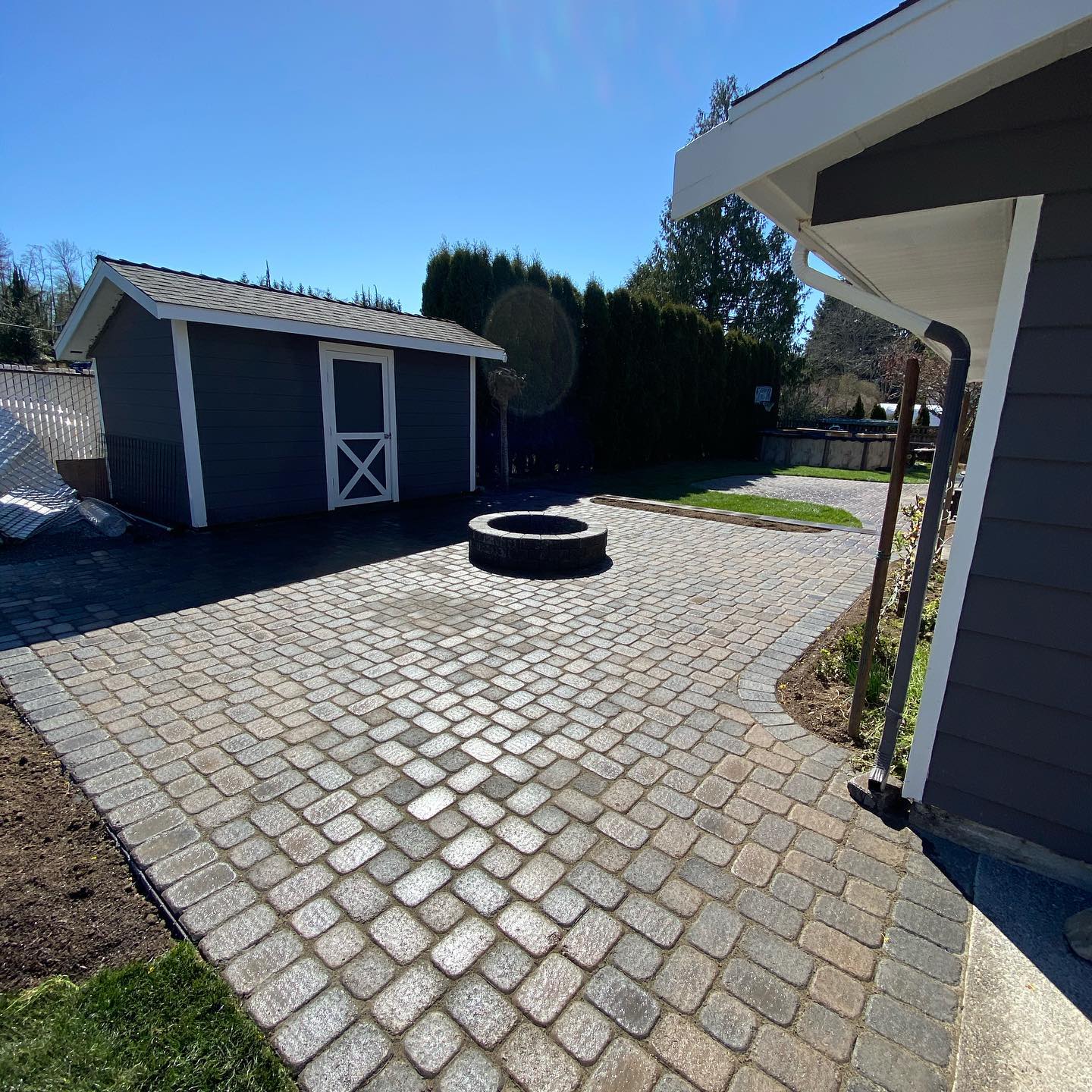 A patio with a fire pit and a shed in the background