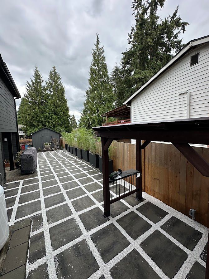 A black and white patio with a wooden pergola in the backyard of a house.