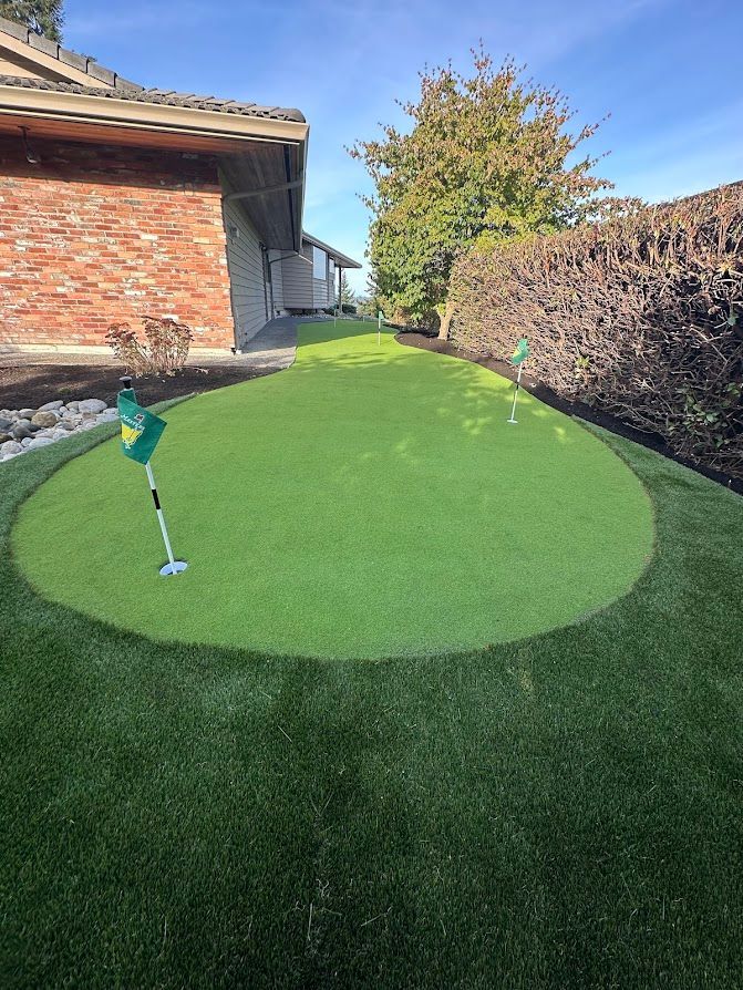 A green putting green in front of a brick house.