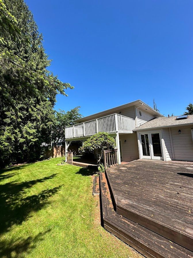 A house with a large deck and a large lawn in front of it.