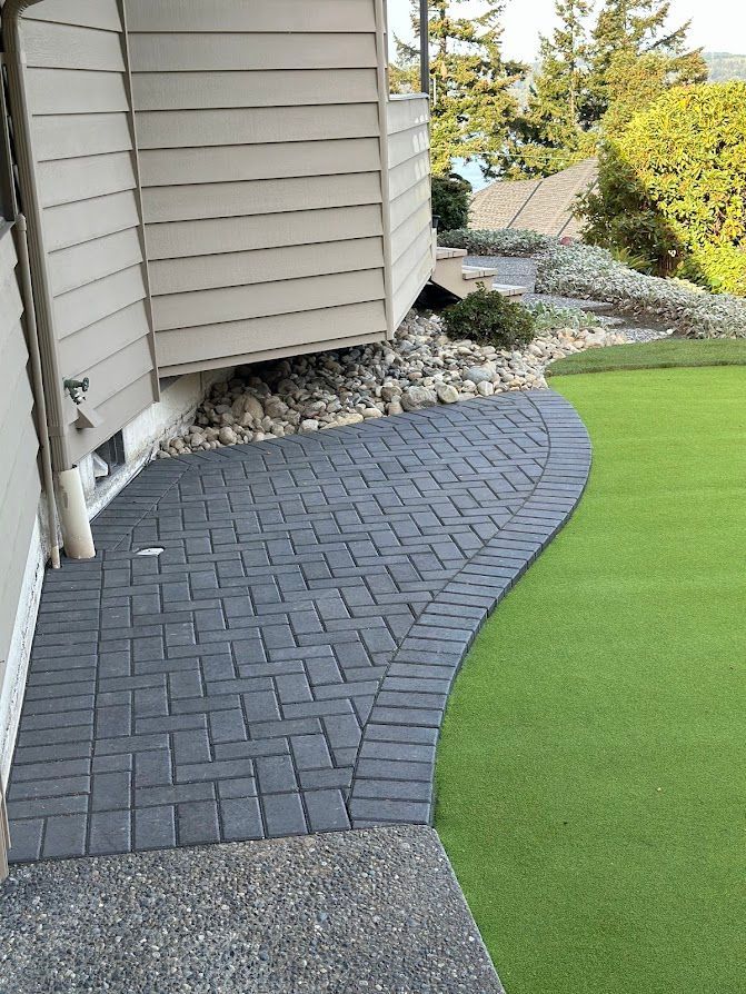 A brick walkway leading to a house next to a green lawn.