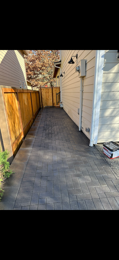 A brick walkway leading to a house with a wooden fence.