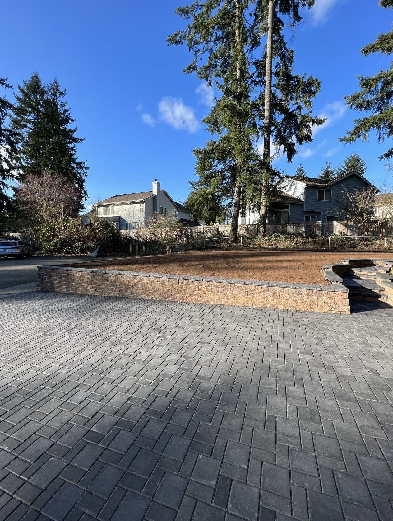 A brick driveway in front of a house with trees in the background.