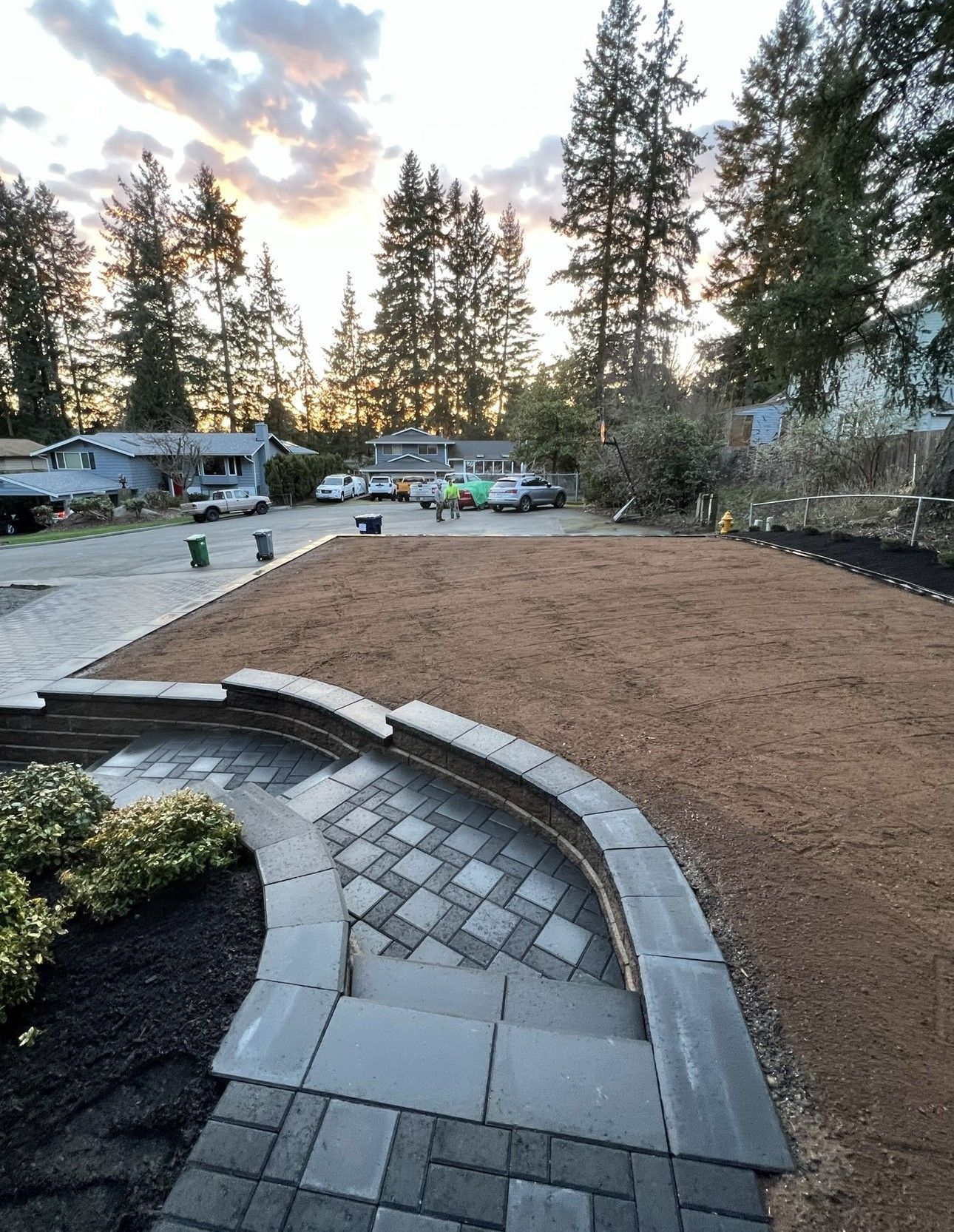 A brick walkway leading to a lush green yard with trees in the background.