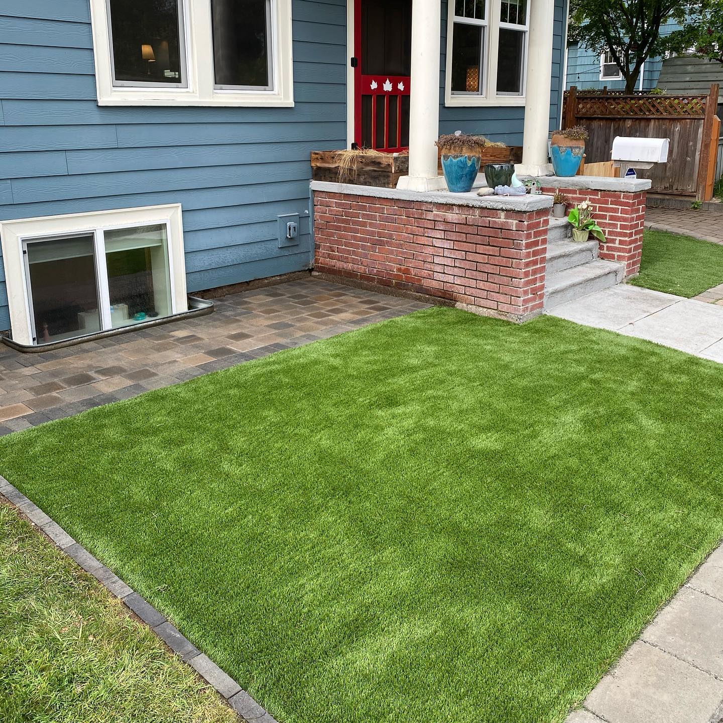 A blue house with a brick porch and a lush green lawn in front of it.