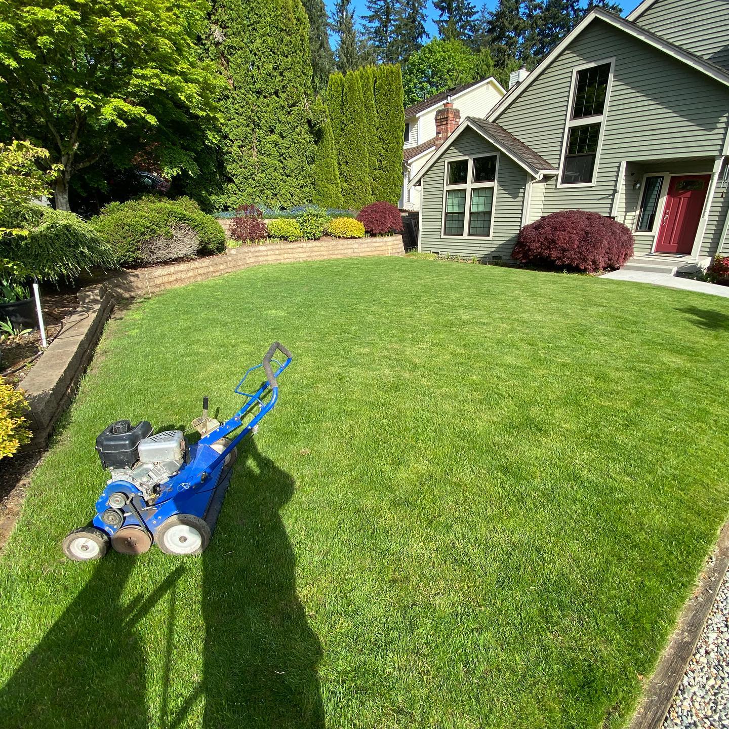 A blue lawn mower is cutting a lush green lawn in front of a house.