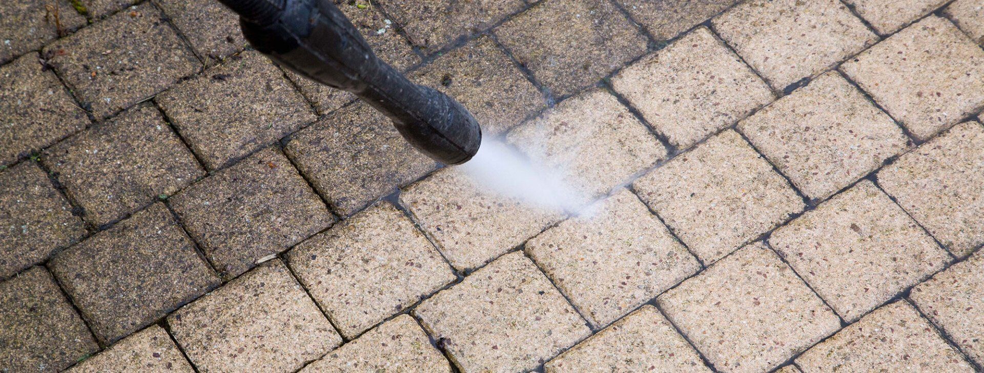 A person is using a high pressure washer to clean a brick walkway.